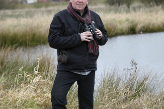 Aidan stands with his binoculars on a reserve