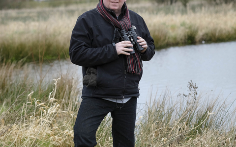 Aidan stands with his binoculars on a reserve