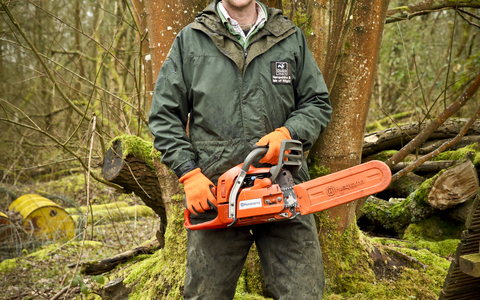 Adam stands with a chainsaw in a wood