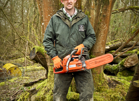 Adam stands with a chainsaw in a wood