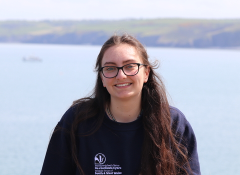 Maddy smiling at the camera, with the sea behind her